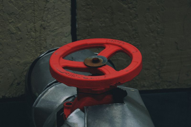 A red handwheel valve on top of a large insulated metal pipe.